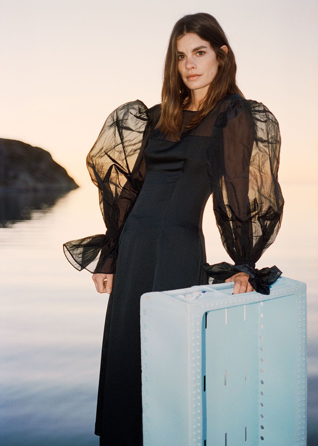 modell som står foran sjøbildet bakgrunn iført en svart kjole med store overdimensjonerte organza puffermer